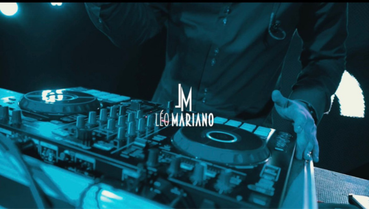 Imagem do DJ Leo Mariano, na mesa de som operando durante evento.